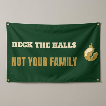 Deck The Halls Not Your Family flag 3x5 in dark green with gold text and a cracked ornament, hung on a wall