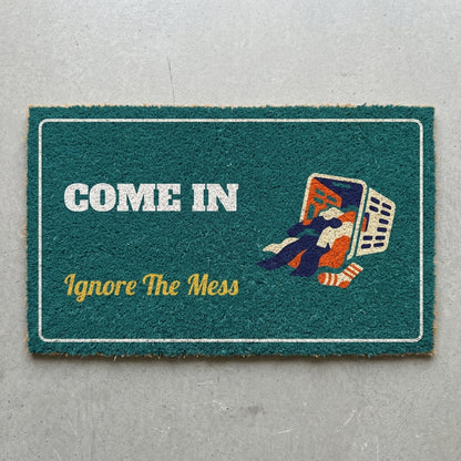 Come In Ignore The Mess doormat 30x18 in teal with a spilled laundry basket