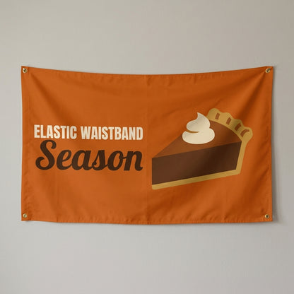 Elastic Waistband Season flag 3x5 in orange with a slice of pie, hung on a wall