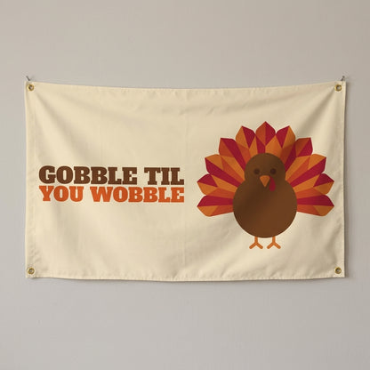 Gobble Til You Wobble flag 3x5 in cream with a cartoon turkey, hung on a wall