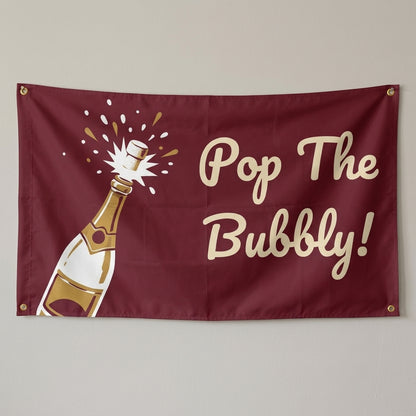 Pop The Bubbly flag 3x5 in burgundy and gold with a popping bottle, hung on a wall